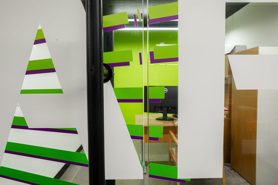 Close view of green and white striped film and large lettering on glass beside a black door pull