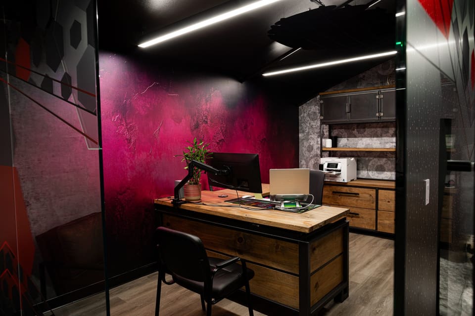 Small office with a magenta textured wall, wood desk and a glass partition