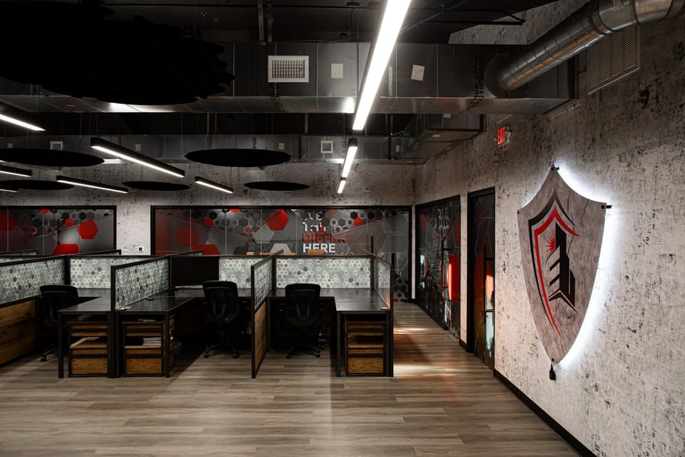 Open office with rows of desks, frosted hexagon-pattern panels and a lit shield logo on the wall