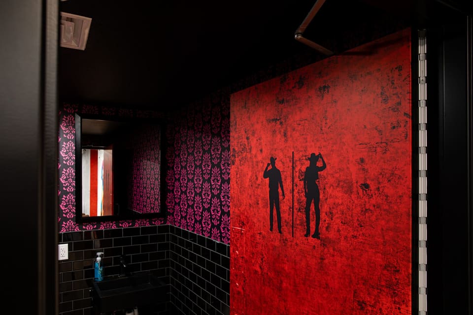 Restroom entry with a bold red printed panel with two silhouettes beside patterned wallcovering