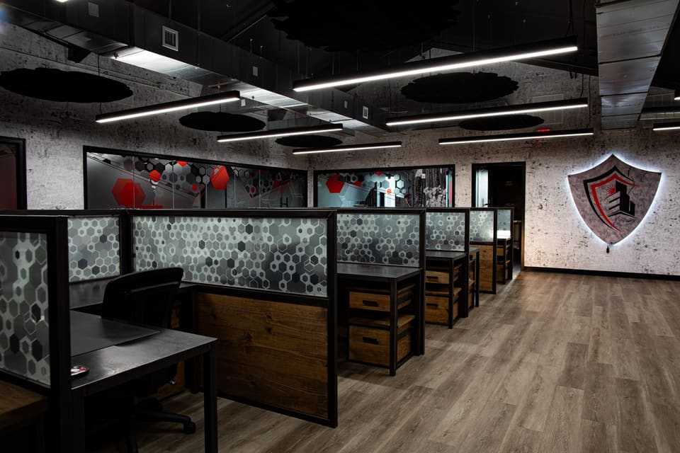 Open office with workstation panels in the foreground and a backlit shield logo on the wall