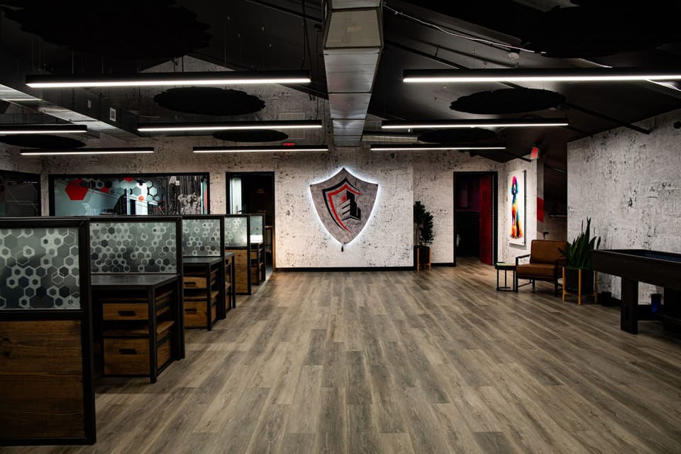 Open office floor with a lit shield logo on the wall and a lounge corner at right