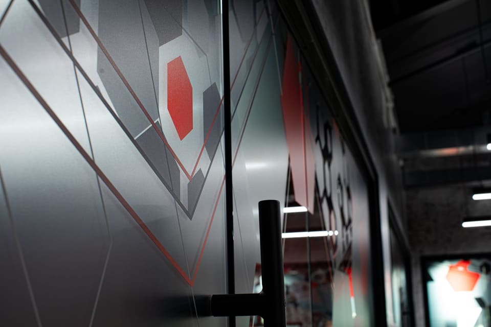 Close view of angled frosted film and thin red lines on a glass door beside a black pull handle