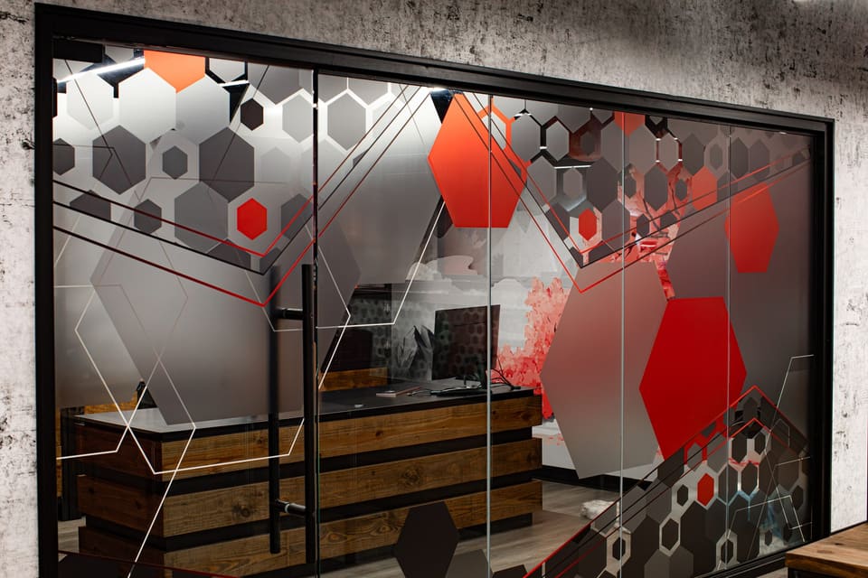 Glass office wall with large red and gray hexagon graphics over frosted film, with a reception desk visible behind
