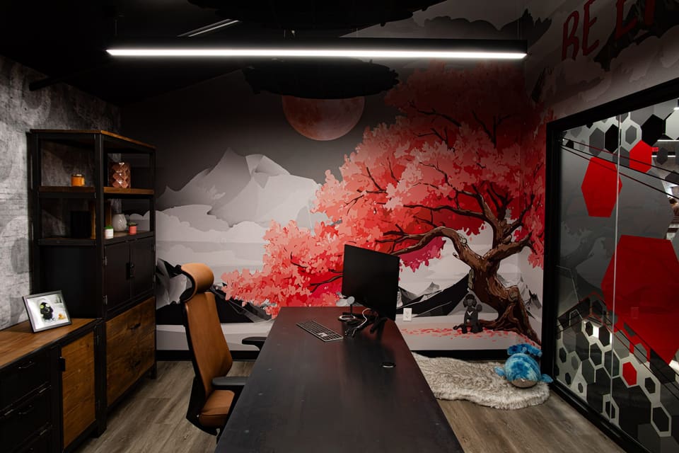 Office with a mural of a red tree behind the desk and shelving to the left