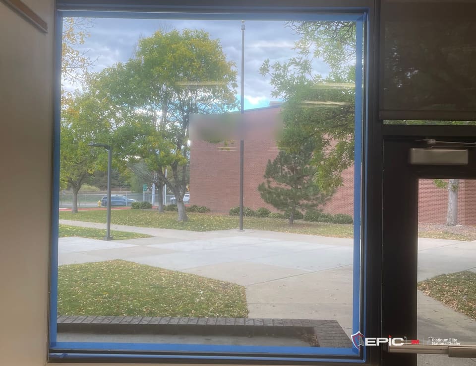 A tall school sidelite taped blue at the frame, lawn, sidewalk and trees outside