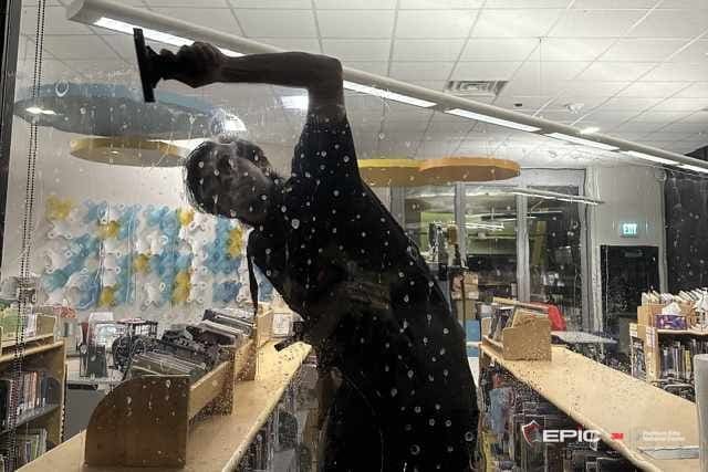 Silhouette of an installer squeegeeing solution from a glass wall in a lit school library after hours