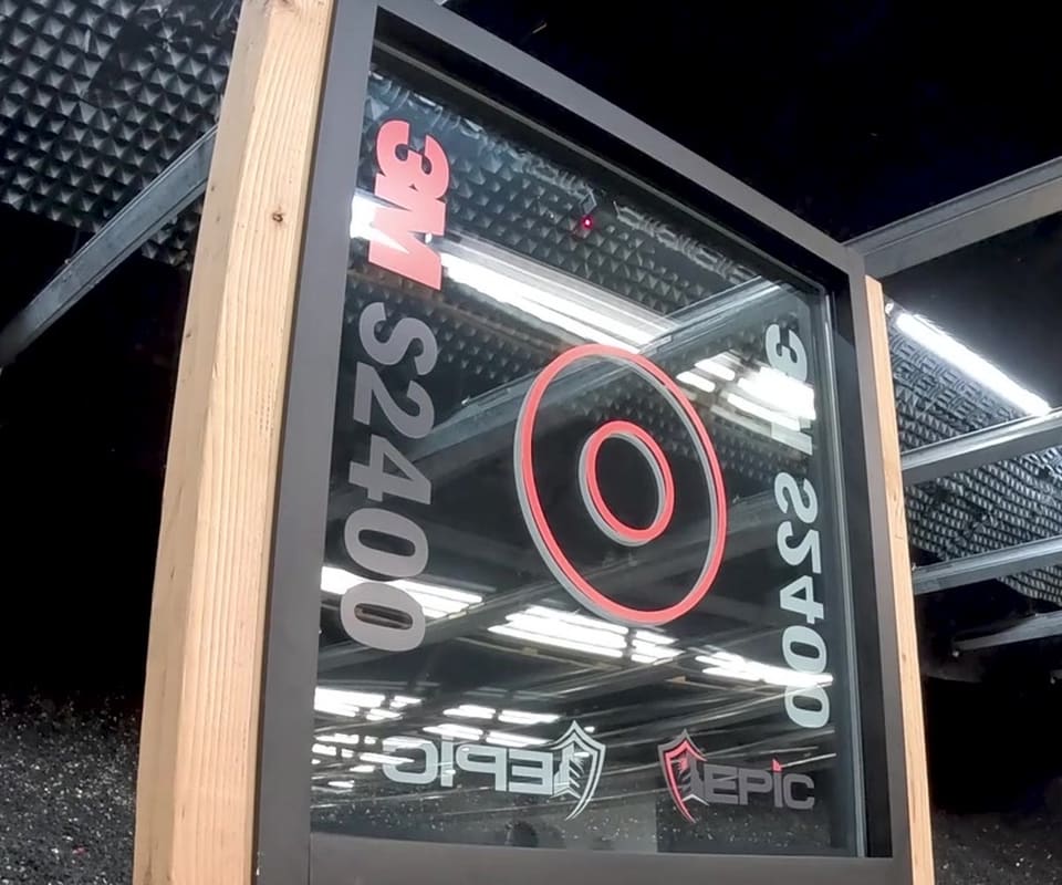 Before: 3M S2400 security film test panel on a wooden stand at Epic’s live demonstration, before and after the impact sequence — the glass shattered but held in the frame