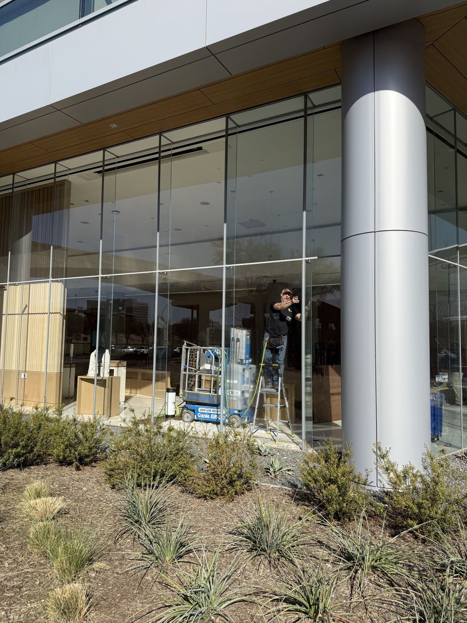 Outside the chapel: a Certified Installation Specialist on a lift working on the tall curtain-wall glass beside a round column