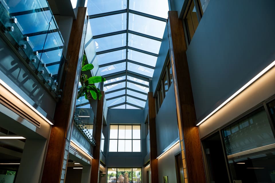 Two-story atrium with tall timber columns, glass railings and a peaked glass skylight overhead, a tall window at the far end