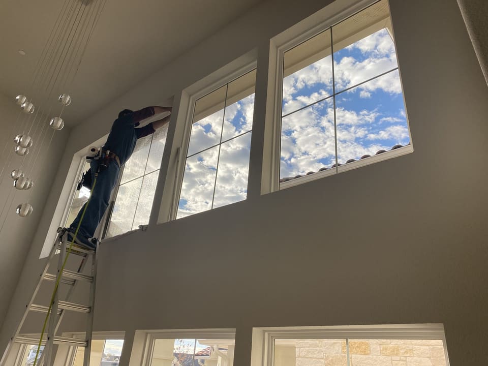 Epic Certified Installation Specialist on a ladder filming two-story living room windows