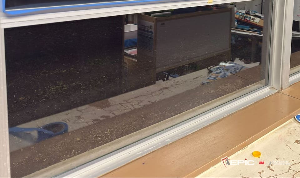 A classroom window's lower lite with a bare aluminum frame, before taping