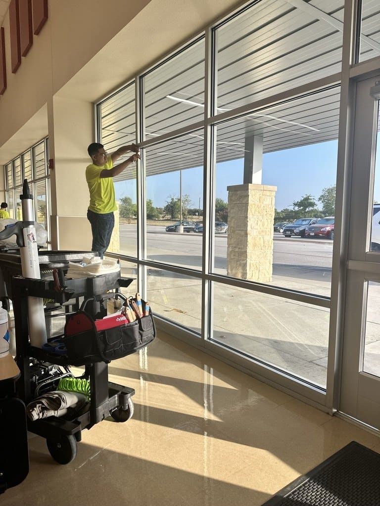 Certified Installation Specialist preparing a window frame on a cafeteria glass wall, a supply cart beside him
